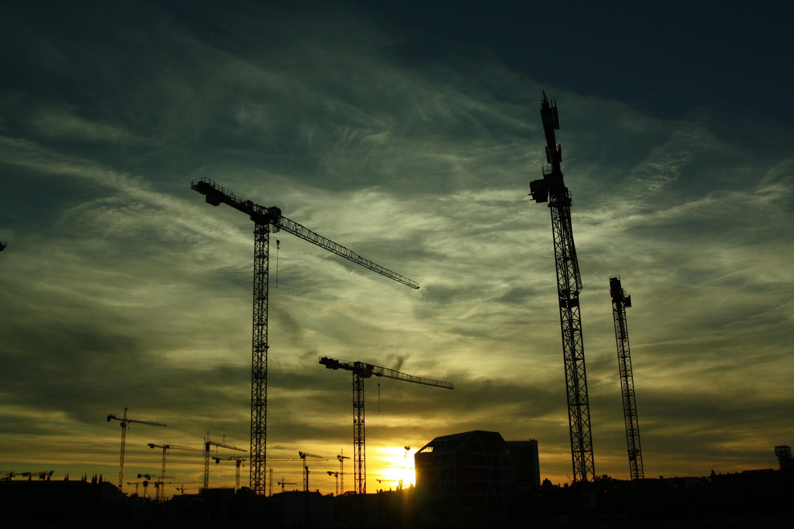 Construction cranes silhouetted against a sunset sky, symbolizing rebuilding and reform in public infrastructure.
